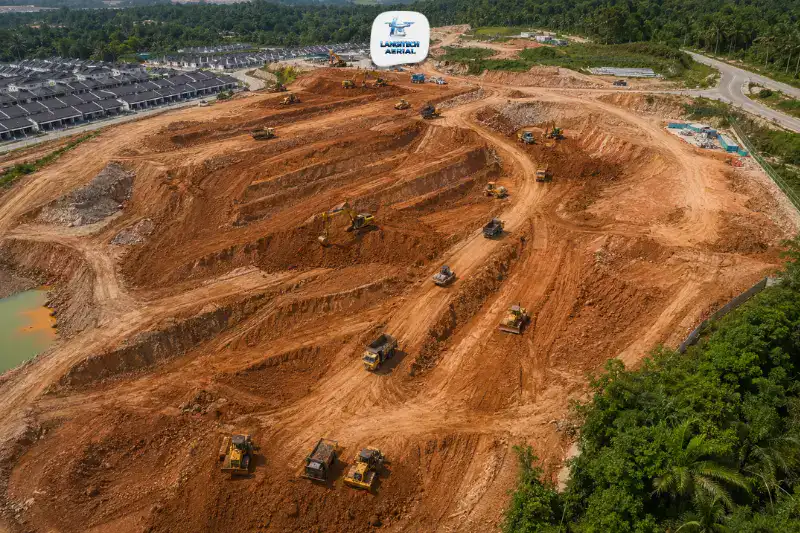 Aerial drone view of Malaysian construction site showing active earthworks grading operations with excavators on red laterite soil